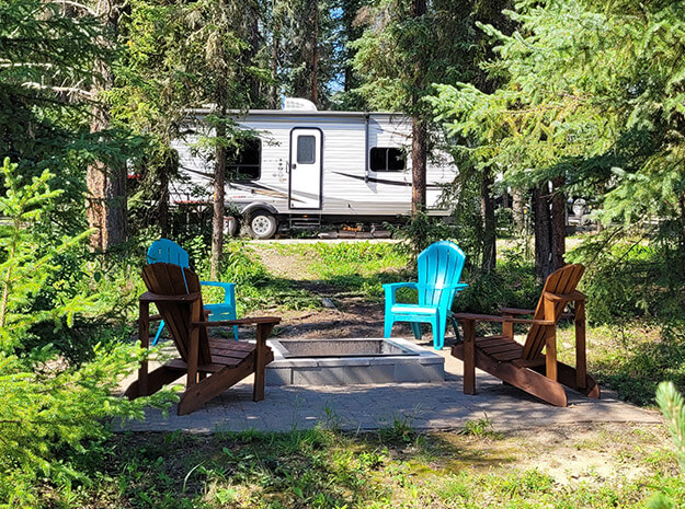 Campsite amongst trees with adirondak chairs in foreground